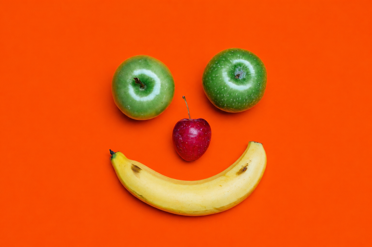 Apples a cherry and a banana used to create a smiling face on an orange background.